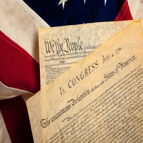 The Declaration of Independencer and the Constitution, with the American flag as background.